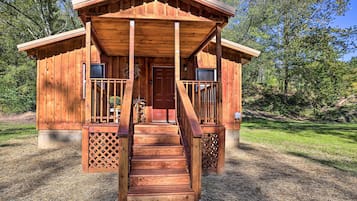 A wooden cabin with a porch, a front door, and a staircase leading up to the entrance.