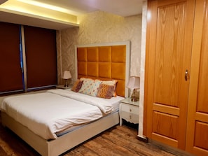 Relax in a spacious room with a large bed, wooden wardrobe, and a nightstand with a lamp.