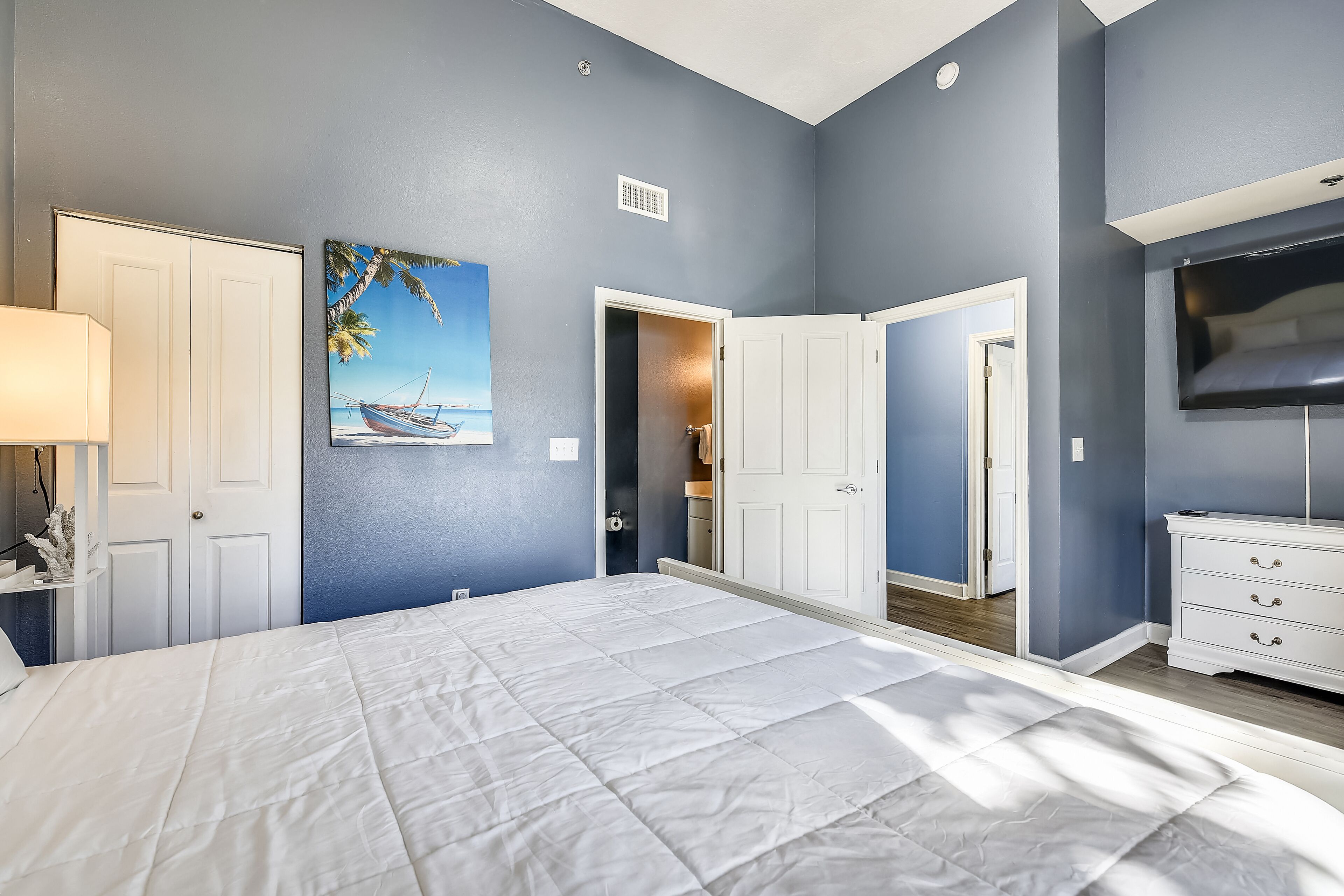 Une chambre à coucher avec un grand lit, une télévision et un tableau représentant une scène de plage.