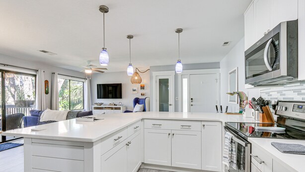 A modern kitchen with white cabinetry, a large island, stainless steel appliances, pendant lighting, and a view of the outdoors. - Walk to Coligny Beach: Tropical Hilton Head Condo (Hilton Head Island)