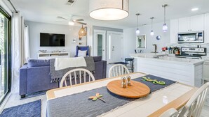 A modern kitchen with white cabinets, a microwave, and a dining area with a wooden table and chairs. - Walk to Coligny Beach: Tropical Hilton Head Condo (Hilton Head Island)