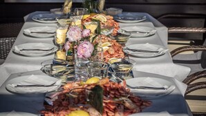 Une longue table à manger, dressée avec des assiettes, des couverts, des verres et une variété de fruits de mer.