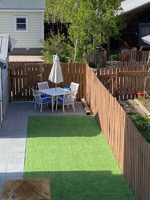 A patio with a table and chairs, a wooden fence, and a green artificial turf area. - The Red Lady, Cute 2BD in Town! (Crested Butte)