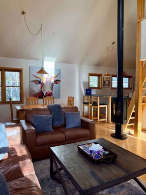 A cozy living room with a brown leather sofa, a wooden coffee table, and a colorful abstract painting on the wall.
