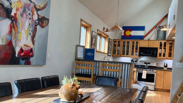 Un vaste espace dédié à la salle à manger, avec une longue table en bois, des chaises noires et un grand tableau représentant une vache accroché au mur.