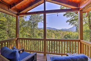 Eine Holzterrasse mit zwei Liegestühlen und Blick auf Wald und Berge.