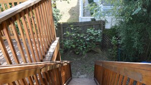 Un escalier en bois descend vers un jardin, qui est délimité par une clôture en bois et agrémenté de verdure.