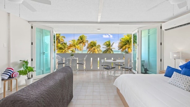 Quarto de hotel com varanda, uma cama, um sofá e um espaço de refeições com cadeiras e uma mesa.