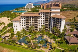 A multi-story hotel with a central pool area, surrounded by palm trees and a view of the ocean. - Beachfront Luxury Community in Ko Olina (Kapolei)