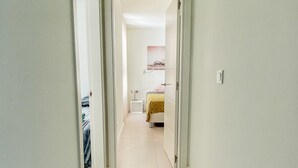 Un pasillo estrecho que desemboca en una habitación con una cama y una mesita de noche.
