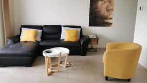 Una sala de estar con un sofá negro, cojines amarillos, una mesa redonda blanca y un sillón amarillo.