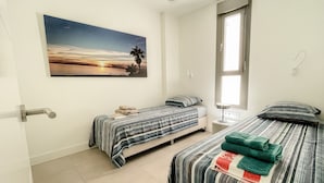 Un dormitorio con dos camas, un cuadro de un atardecer, una ventana y una puerta.
