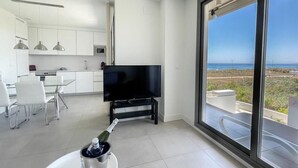 Una cocina moderna con armarios blancos, un televisor de pantalla plana y un comedor con sillas blancas.