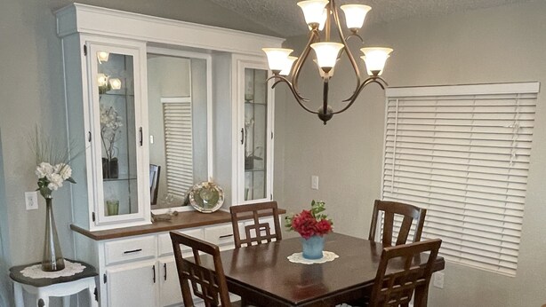 A dining area with a wooden table, four chairs, a chandelier, a small side table with a vase, and a cabinet with glass doors. - Desert Hideaway (Glendale)