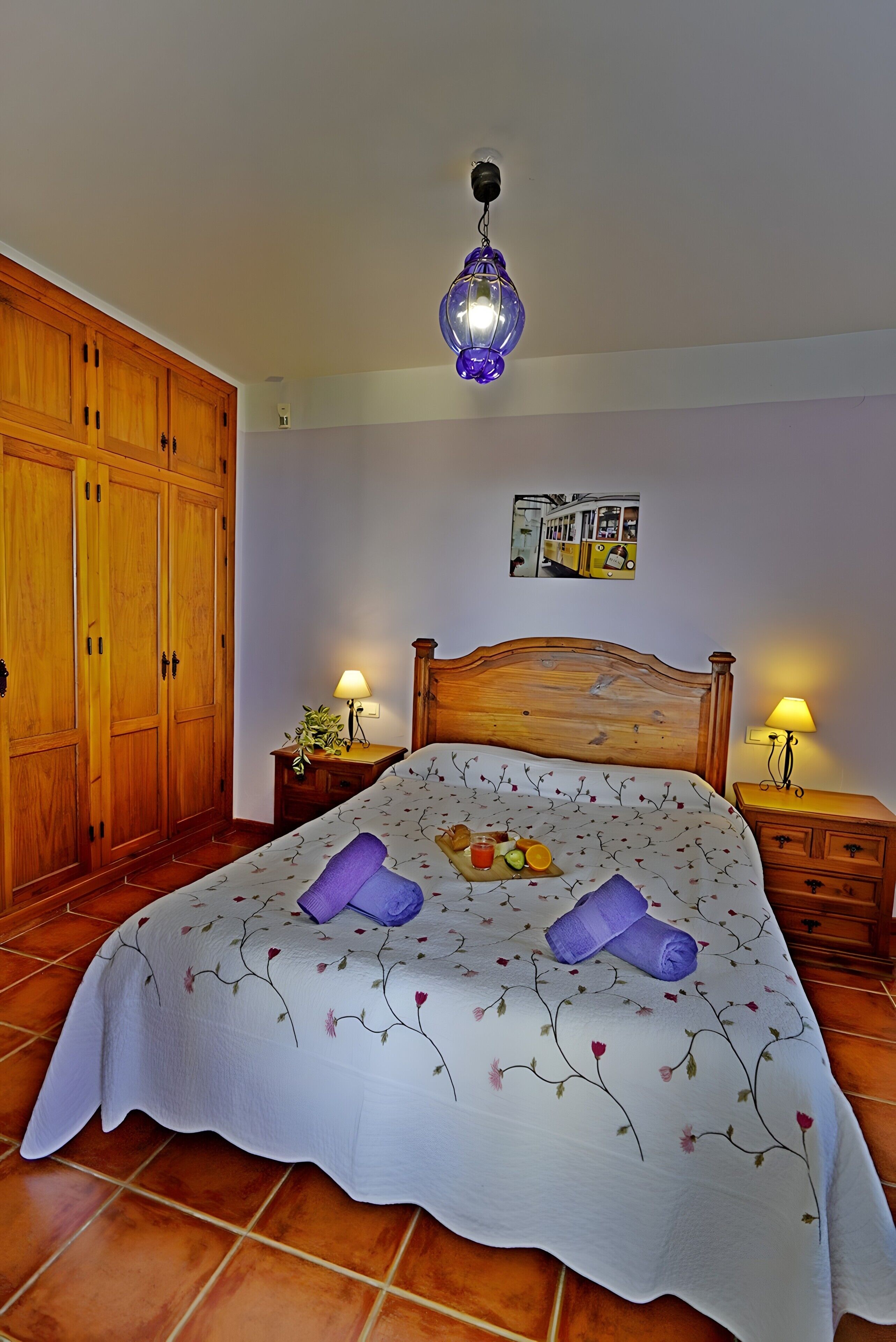 Een slaapkamer met een houten bed, twee nachtkastjes met lampen, een grote kledingkast en een hanglamp.