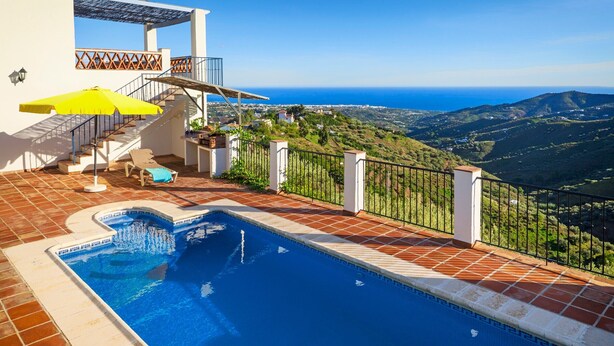 Una piscina con vista sul mare, una scala e una terrazza con un ombrellone giallo.