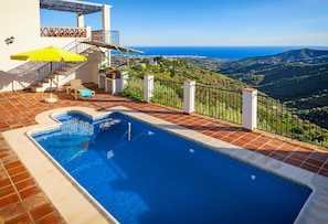 A swimming pool with a view of the sea, a staircase, and a terrace with a yellow umbrella.