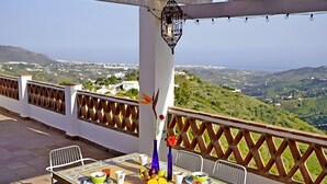 Una terrazza esterna con un tavolo apparecchiato per la colazione, sedie, una lanterna pensile e vista sulla campagna.