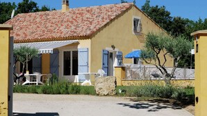 A yellow building with a red-tiled roof, a covered patio with outdoor seating, and a stone wall with a metal gate.