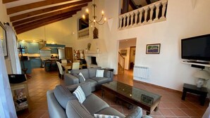 A spacious living room with a large grey sofa set, a glass coffee table, and a flat-screen TV mounted on the wall.