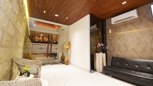 A modern lobby with a wooden ceiling, a black leather sofa, wicker chairs, and a marble floor.