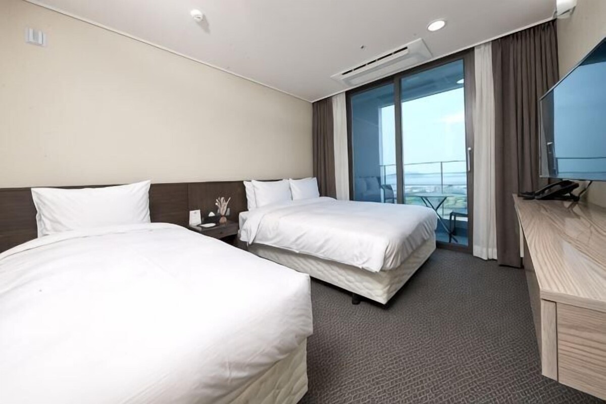Ein Hotelzimmer mit zwei Betten, einem Schreibtisch, einem Stuhl und einem großen Fenster.