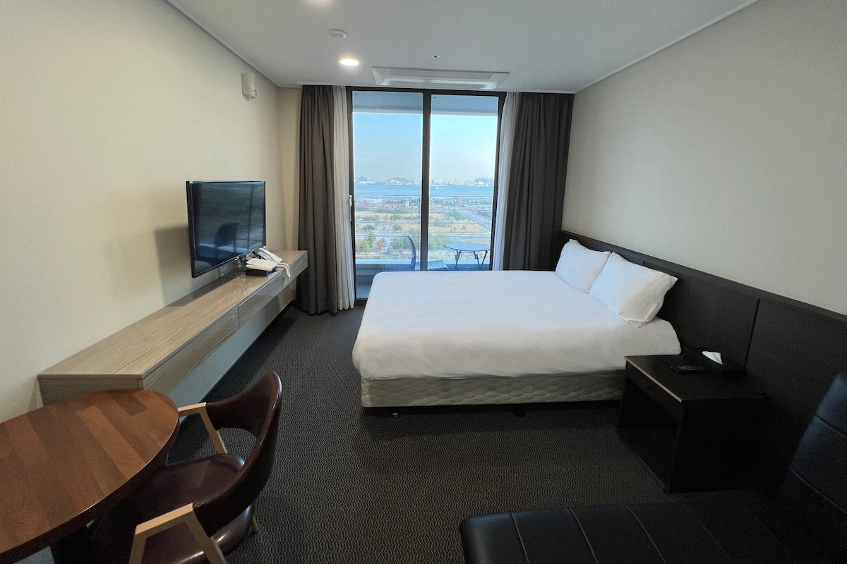 A hotel room with a large bed, a TV, a desk, and a chair.