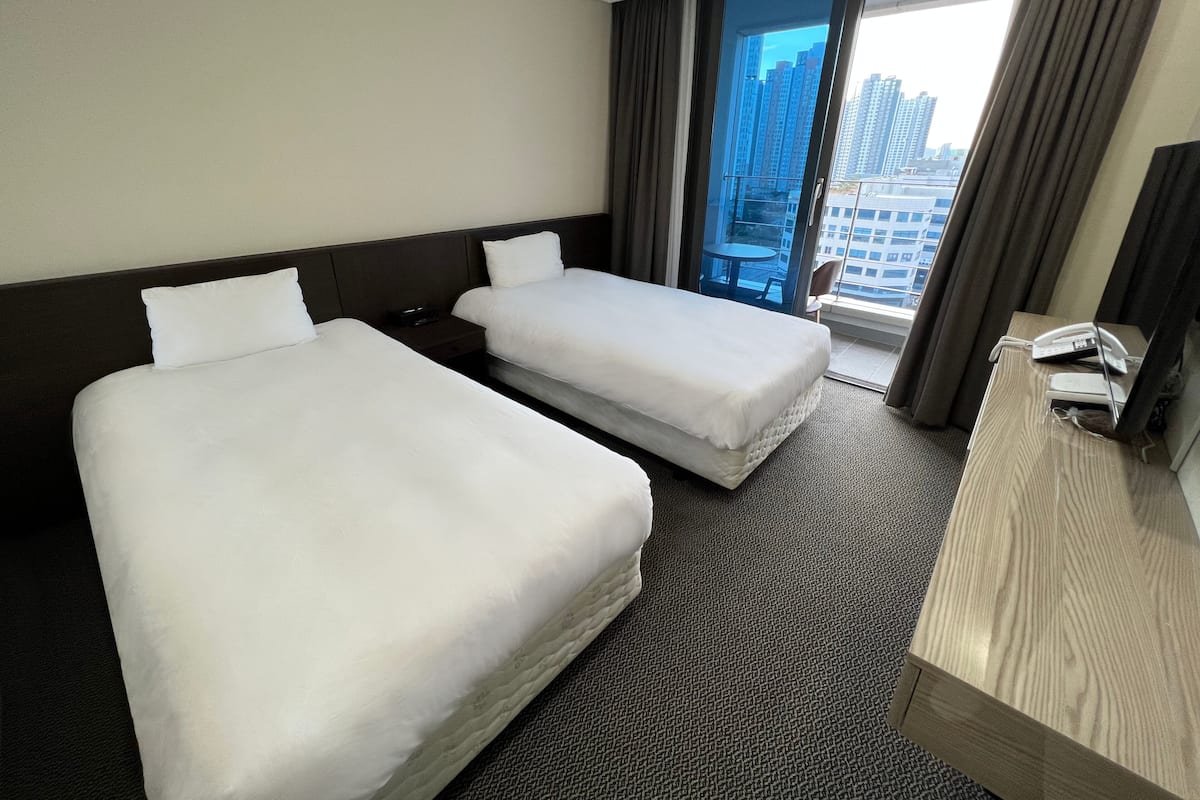 A hotel room with two beds, a desk, and a view of tall buildings.