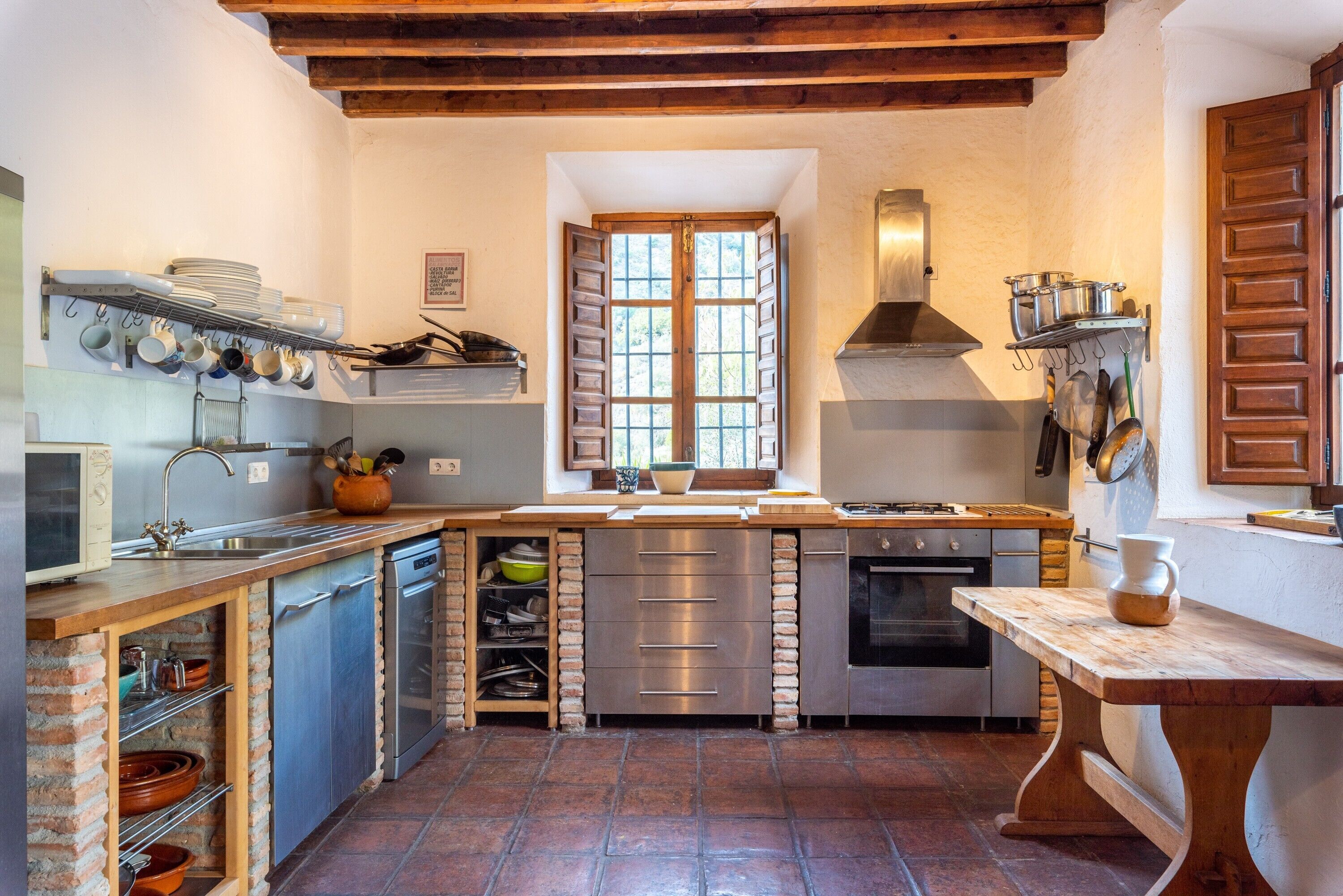Une cuisine avec un plafond en bois, une grande fenêtre et un sol en pierre.