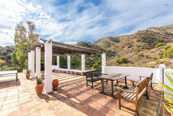 Eine Terrasse mit einer Pergola, Sitzgelegenheiten und Topfpflanzen.