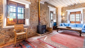Una habitación rústica con paredes de piedra, una silla de madera, un sofá, una chimenea y un tapete rojo estampado.