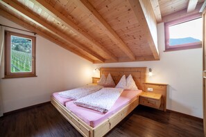 Una camera da letto con soffitto in legno, un letto con cuscini, un comodino e una finestra vista verde.