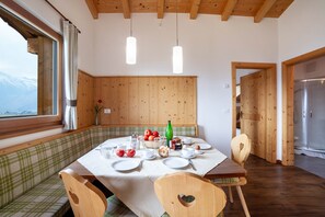 Zona pranzo con tavolo imbandito per quattro persone, pareti in legno, vista sulle montagne e soffitto in legno.