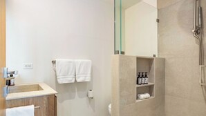 A modern bathroom with a glass shower enclosure, a wooden vanity, and a shelf with toiletries. - Tyrolean 6 | Newly Updated 4BR Condo Steps to Vail Village (Vail)