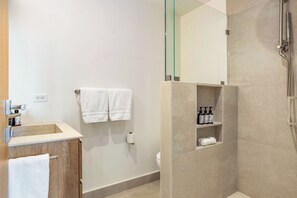Een moderne badkamer met een douchecabine van glas, een houten wastafelmeubel en een plank met toiletartikelen.