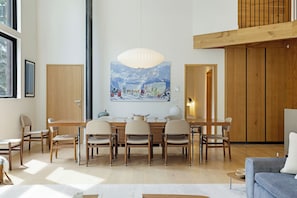 Un vaste espace dédié à la salle à manger, avec une table et des chaises en bois, un grand tableau accroché au mur et une vue sur l’extérieur par une fenêtre.