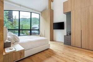 Een moderne slaapkamer met een groot raam, een bed, een nachtkastje, een flatscreen televisie en houten kasten.