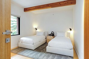 Une petite chambre moderne avec deux lits, une fenêtre et une poutre en bois au plafond.
