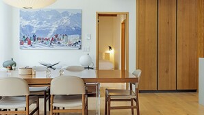 A modern dining area with a wooden table, chairs, and a large mountain landscape painting. - Tyrolean 6 | Newly Updated 4BR Condo Steps to Vail Village (Vail)