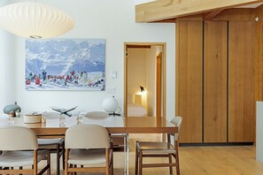 Een moderne eetruimte met een houten tafel, stoelen en een groot schilderij van een berglandschap.