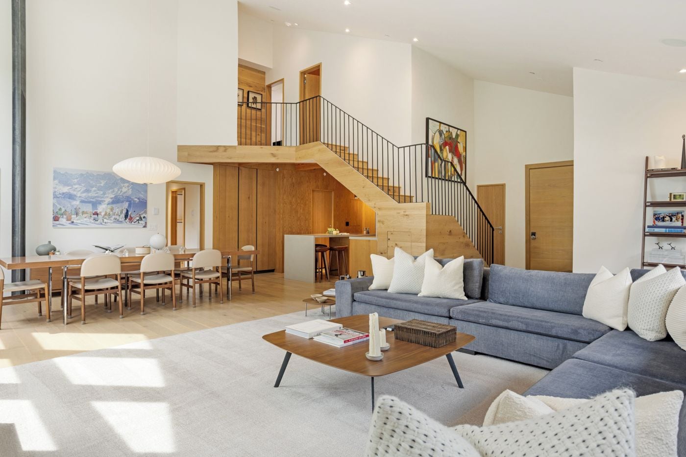 Amplia sala de estar con un sofá azul, una mesa de comedor de madera y una escalera que sube a un nivel superior.