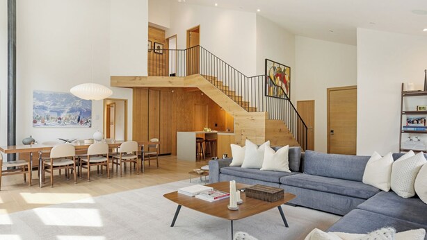 A spacious living area with a blue sofa, wooden dining table, and a staircase leading to an upper level. - Tyrolean 6 | Newly Updated 4BR Condo Steps to Vail Village (Vail)