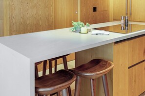 Une cuisine moderne avec un plan de travail blanc, des tabourets en bois et un meuble en bois.