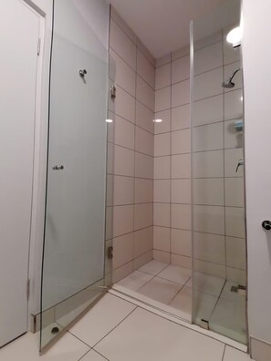 A modern bathroom with a glass shower enclosure, white tiled walls, and a door with a handle.