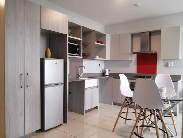 A modern kitchen with built-in appliances, a dining area with white chairs, and a red accent wall.