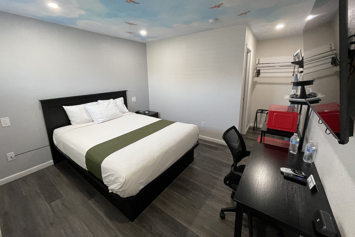 A hotel room with a bed, desk, chair, and a ceiling mural.