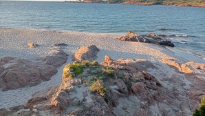 Kivikkoinen ranta, jossa vesi on kirkasta ja kauempana näkyy kukkuloita.