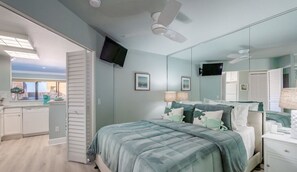 A bedroom with a bed, bedside tables, a mirror, and a television on the wall.