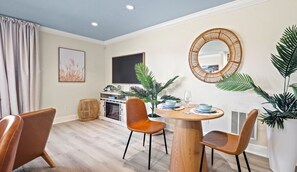 A modern dining area with a round wooden table, two chairs, and a decorative mirror on the wall.