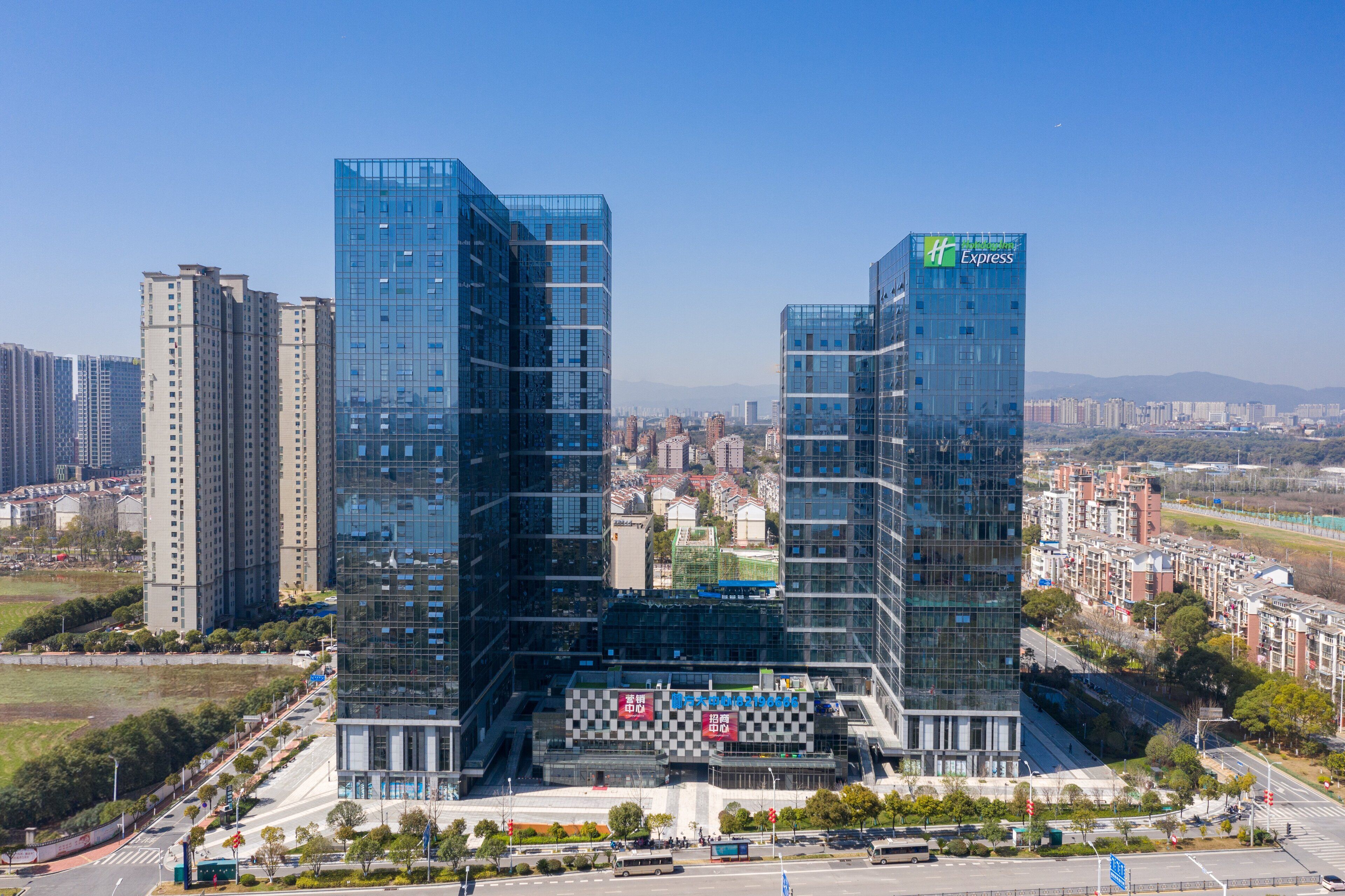 A modern hotel with a glass facade, located in a cityscape with surrounding high-rise buildings.